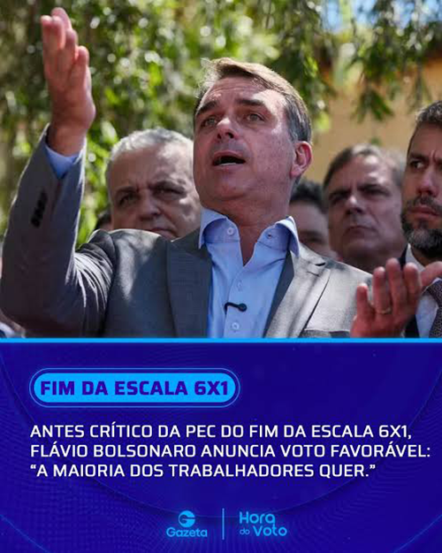 Man in a suit raising his right hand and speaking at a campaign rally with a blue banner reading FIM DA ESCALA 6X1 in the foreground